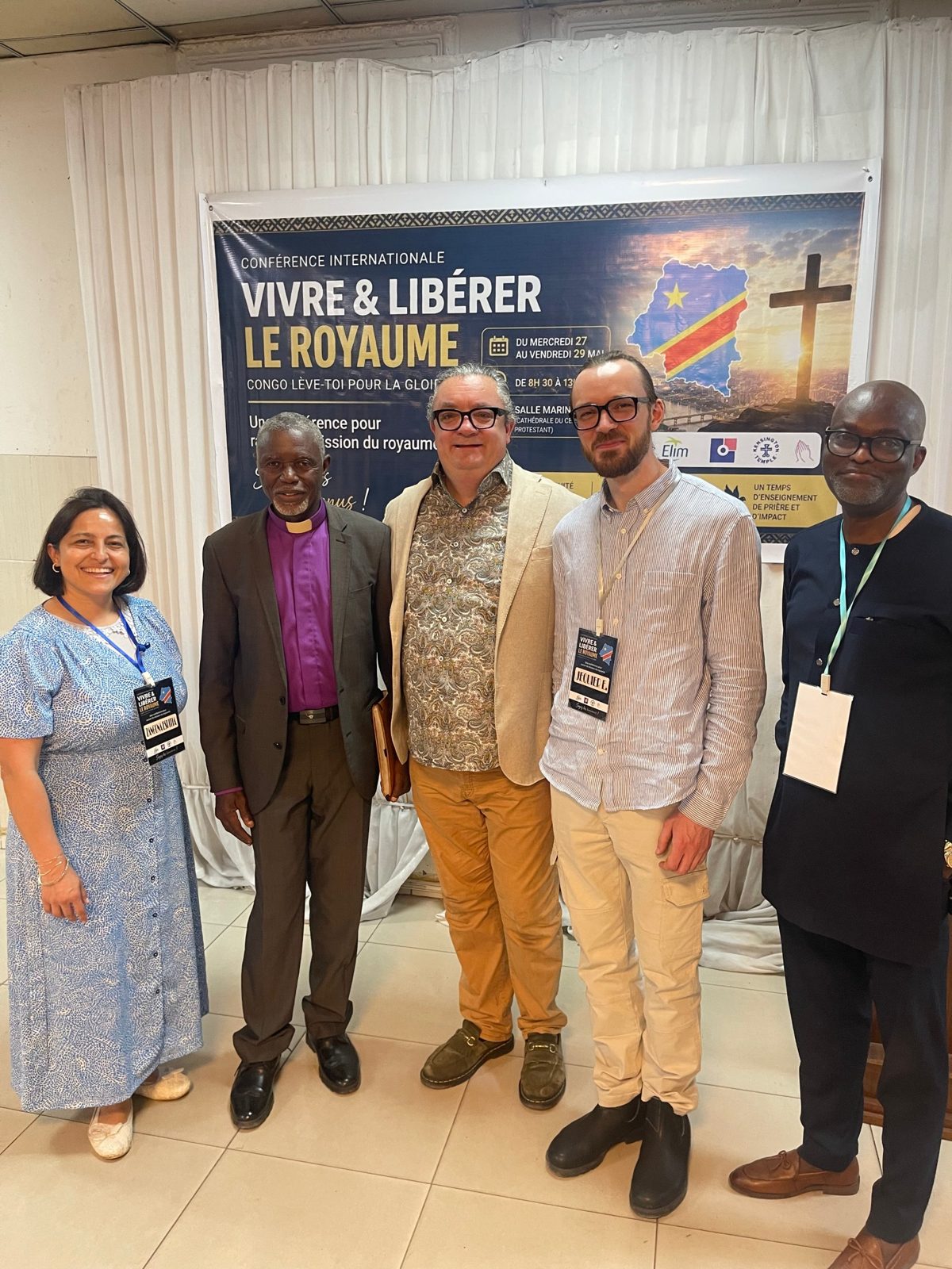Speakers and a local bishop in front of the banner for the conference “Vivre & libérer le Royaume”