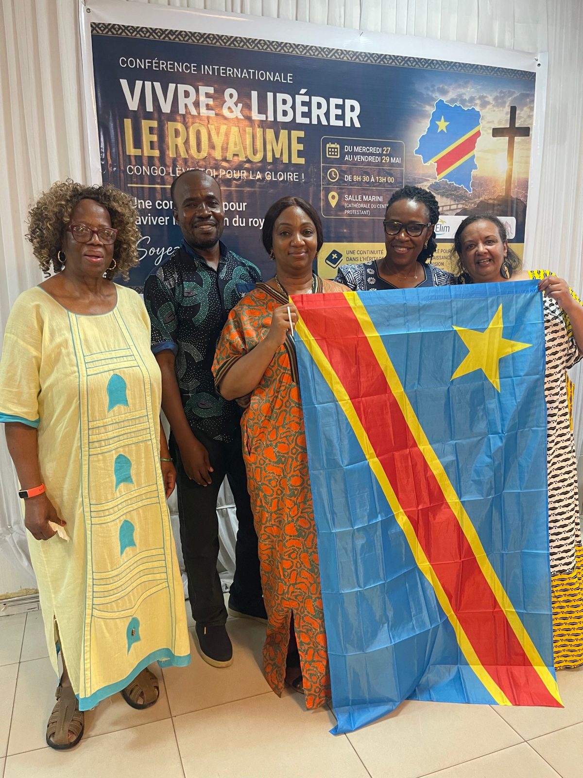Team members holding the flag of the DR Congo in front of the conference banner